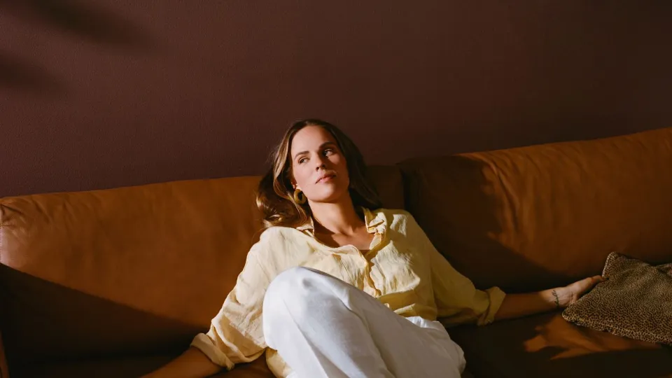 woman relaxing on brown leather sofa and warm brown wall colour in background